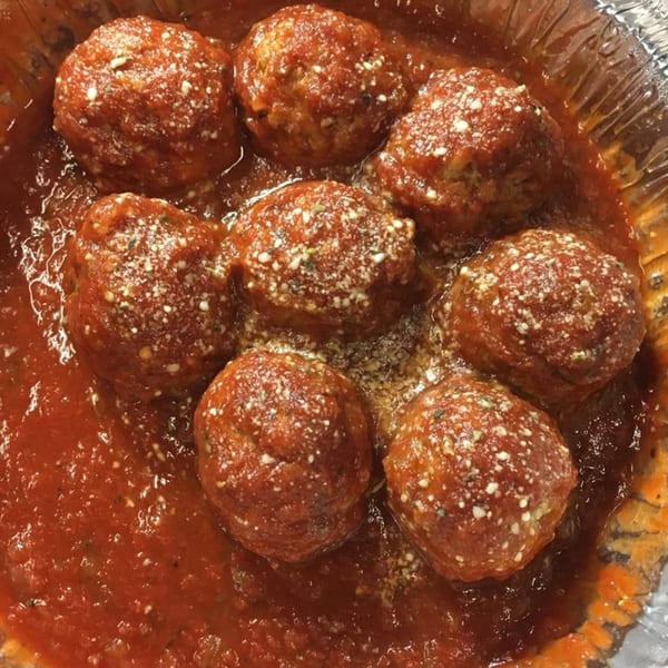 Seven meatballs in a foil container, covered in red sauce and sprinkled with cheese.